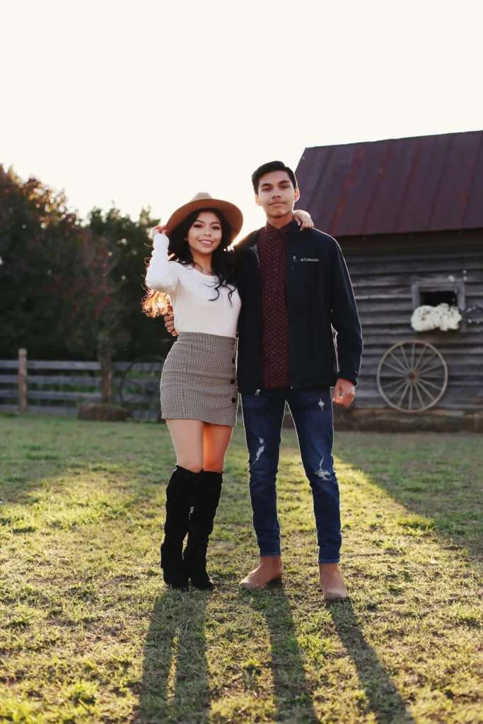 Couple wearing fall outfits with a plaid mini skirt, white fitted top, tan wide-brim hat, black over-the-knee boots, burgundy patterned shirt, and navy jacket.