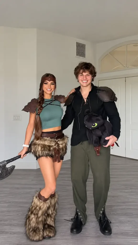 Couple dressed as Hiccup and Astrid with Viking-inspired armor, fur details, and a Toothless plush.