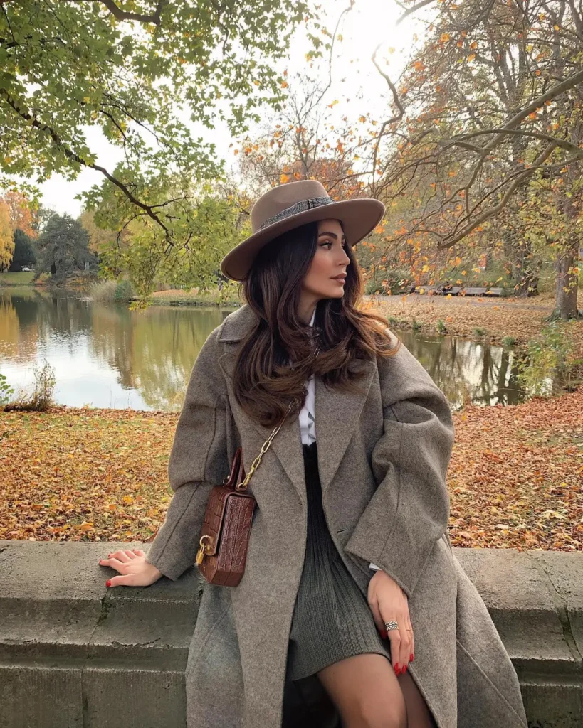 Oversized gray coat worn over a gray mini skirt with white shirt, brown wide-brim hat, and brown crossbody bag.