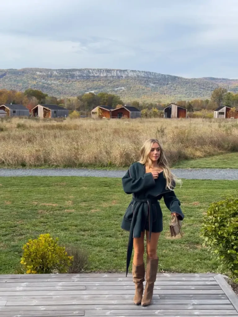 Woman wearing a belted dark forest green short coat with taupe knee-high boots and a small neutral handbag for a refined countryside fall look.
