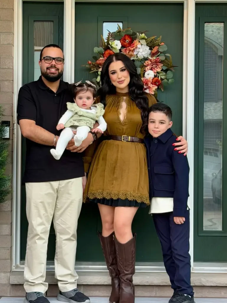 Family wearing coordinated fall outfits with Mom in a mustard belted dress and brown boots, Dad in a black polo and cream trousers, a son in navy, and baby in pale sage green.