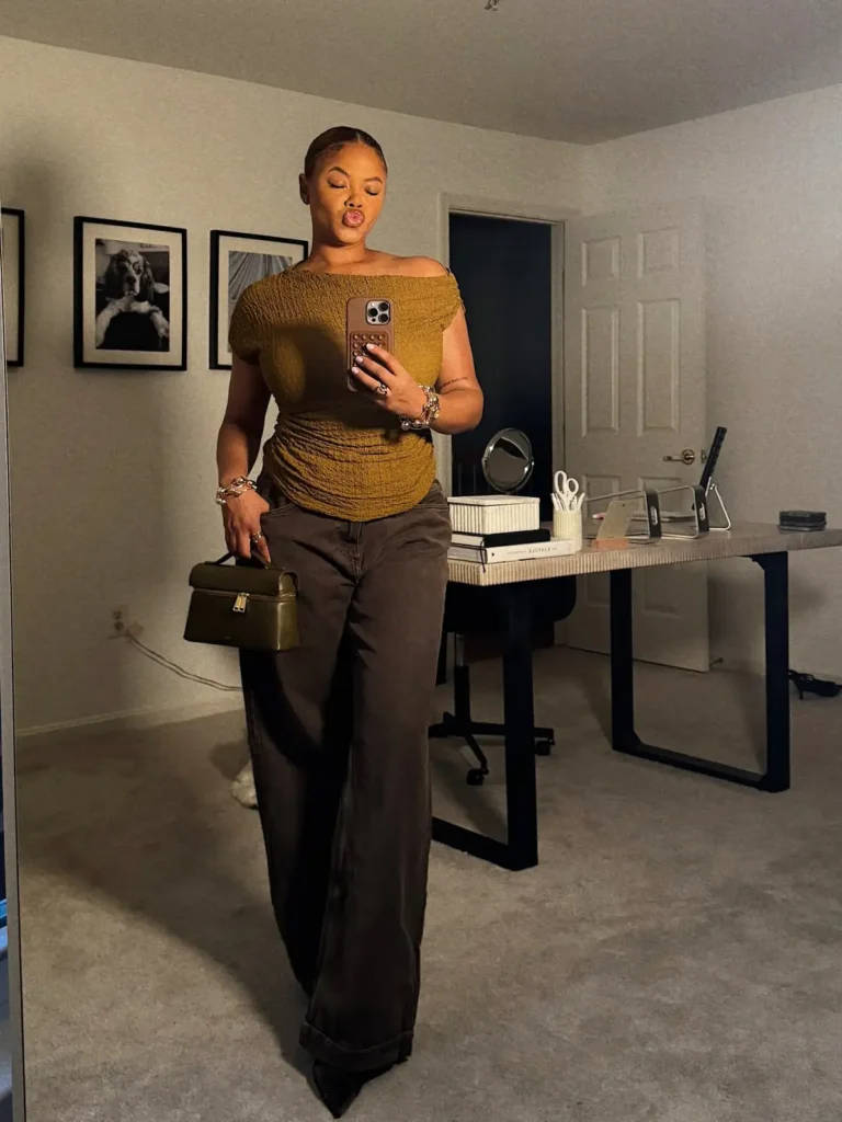 Plus size Black woman wearing a mustard off-shoulder top with dark wide-leg jeans and an earthy structured handbag for a warm fall look.